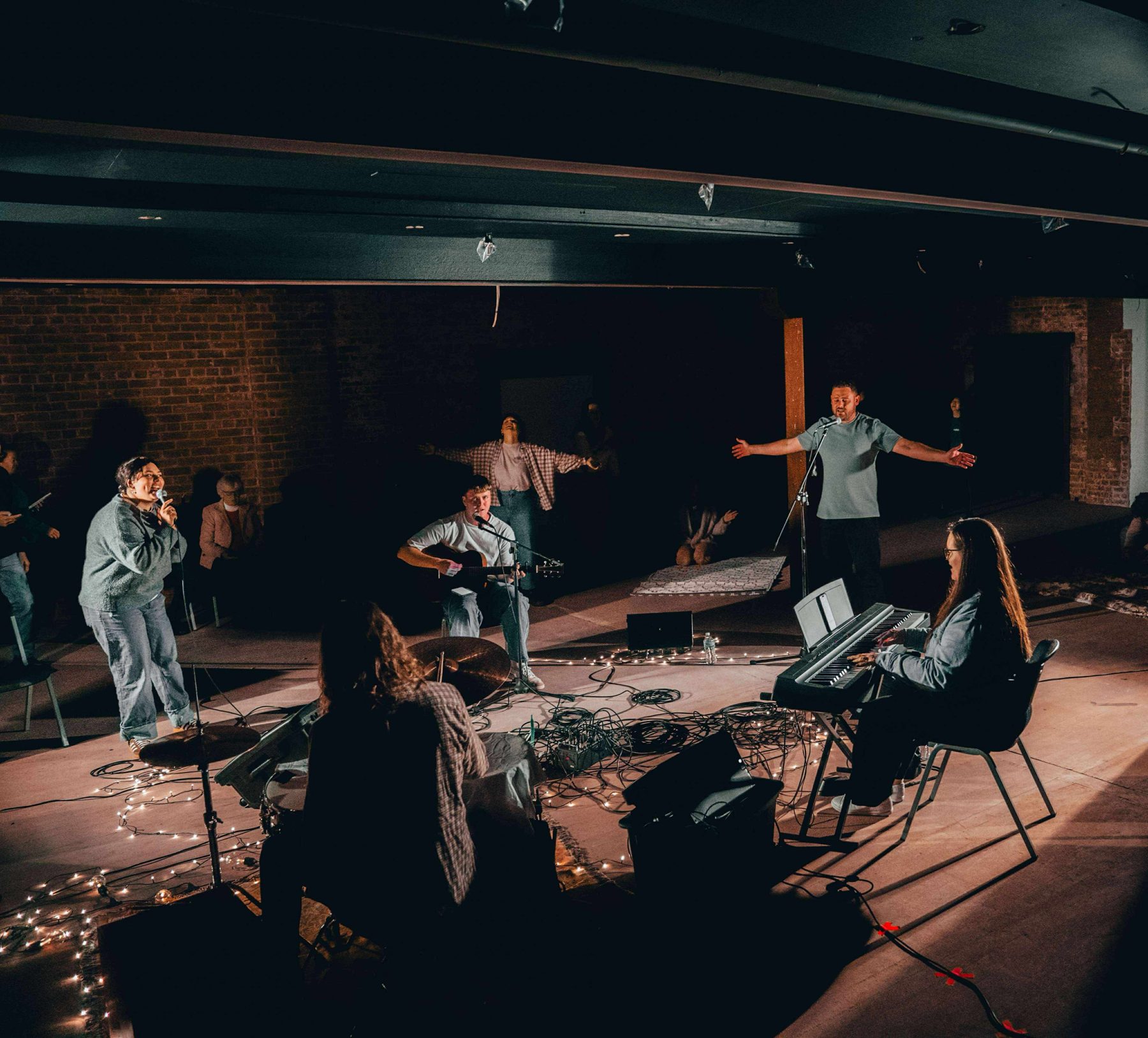 Joshua leading a band in a warmly lit room with keys, guitar and vocals