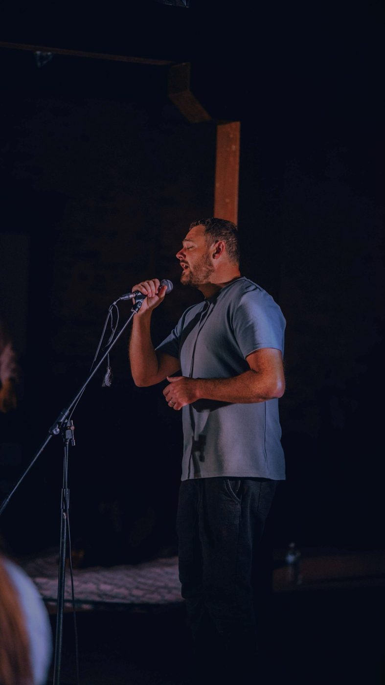 Joshua singing into a microphone on a dimly lit stage
